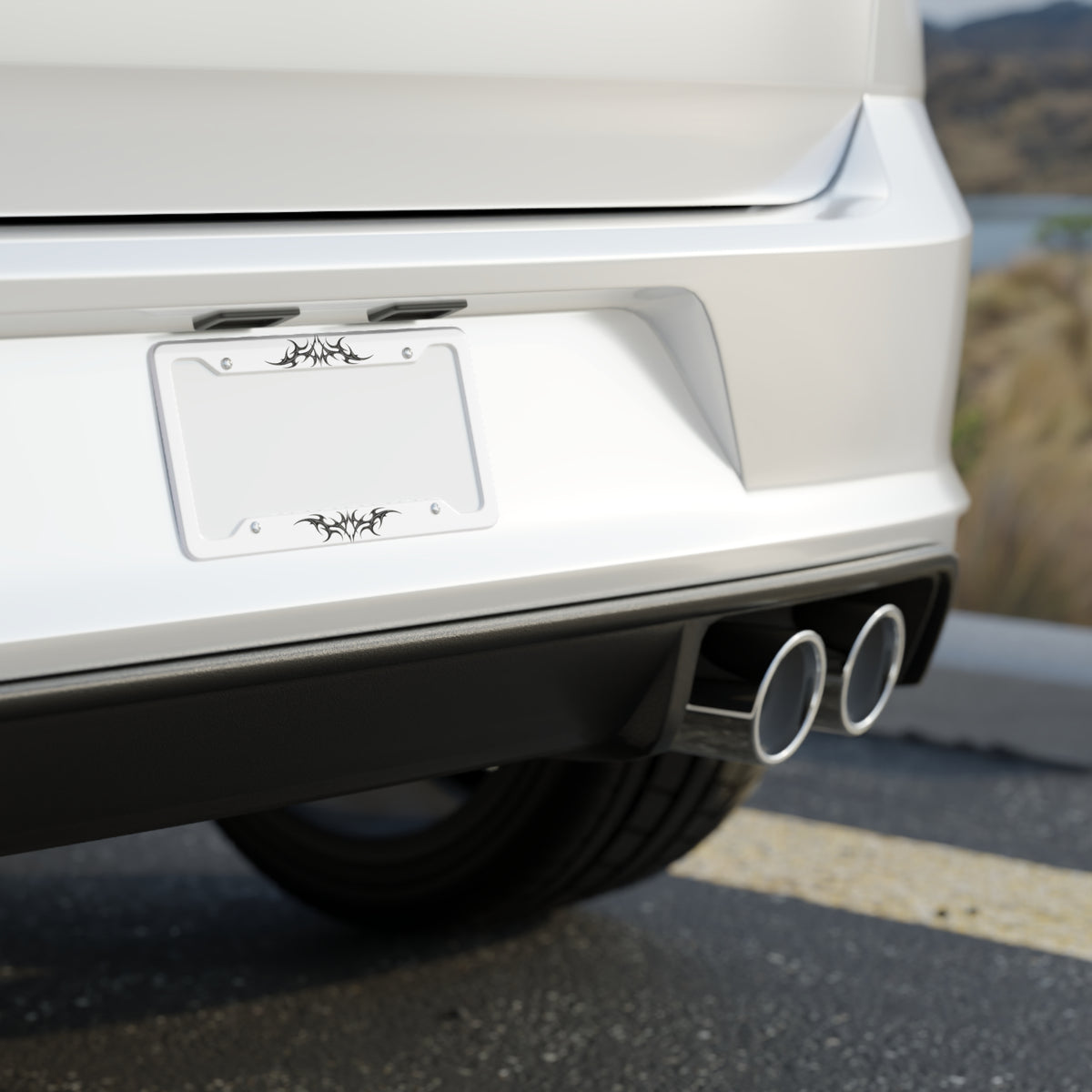 Close-up of a car's rear bumper with a visible license plate on a road. A white license plate frame with black cybersigilism graphic designs on the top and bottom edges.