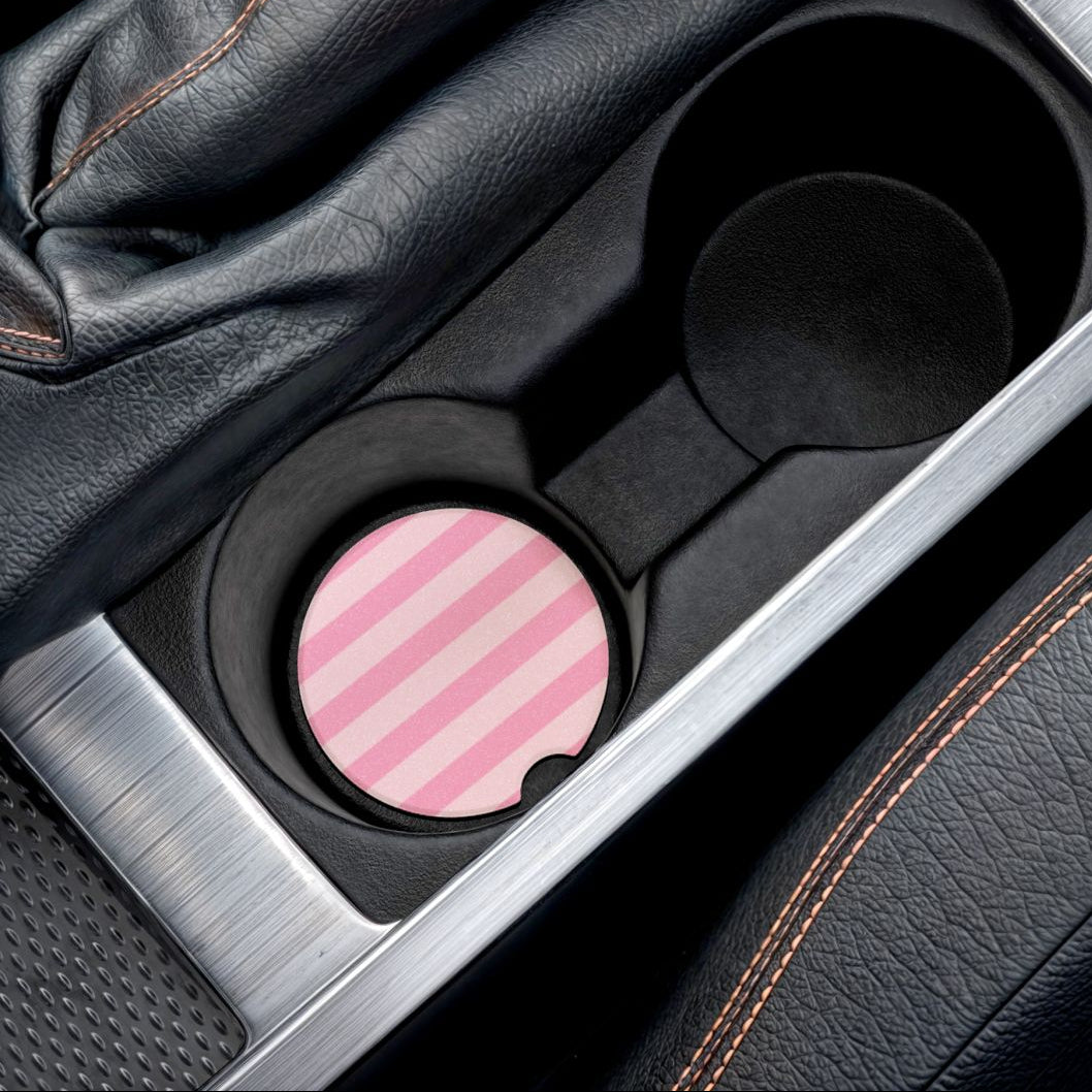 A close-up of a car center console showing a circular pink and white striped cup holder insert in a black cup holder, alongside a black leather gear shift boot and silver trim.